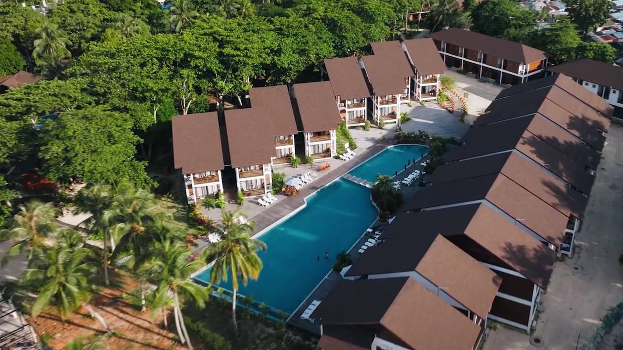 Aerial view of Borneo Divers Mabul Resort: a pool between rows of brown-roofed chalets and tall trees (placeholder, to recheck when the photo is replaced)