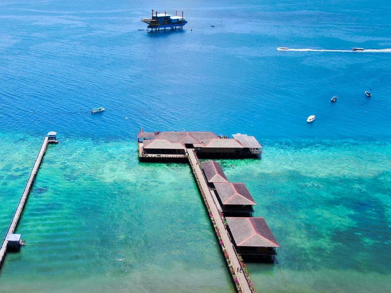 Aerial view of a long jetty running from a white beach out over turquoise water, with a boat beyond (placeholder, to recheck when the photo is replaced)
